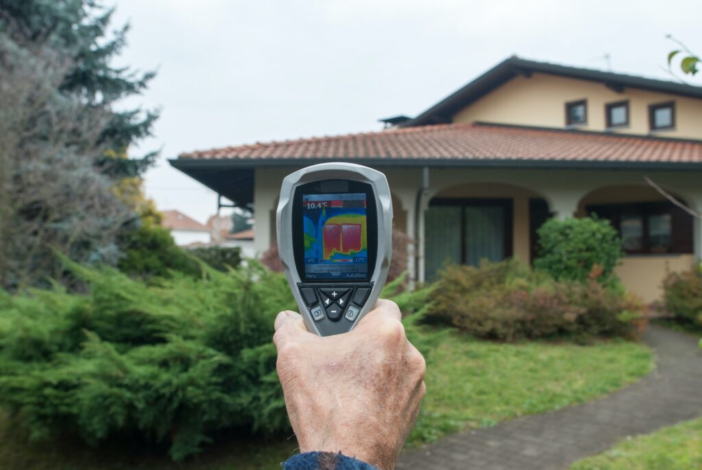 A man demonstrating thermal insulation with an infrared thermometer in front of a house.